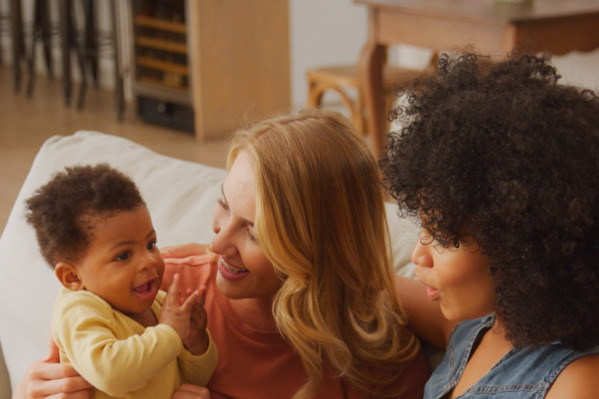 Two mothers laughing with their baby at home